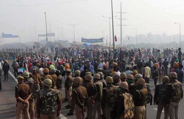 Security personnel look on as farmers block a highway during a protest against newly passed farm bills, at the Delhi-Uttar Pradesh border in New Delhi, December 8, 2020.